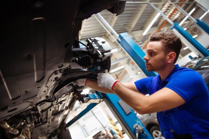 Cheerful, handsome, and confident car repair specialist in overalls repairs and replaces old parts with new ones in a car on a lift in service