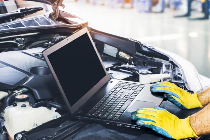 Technician tuning engine car with the computer laptop in repair garage,blank display