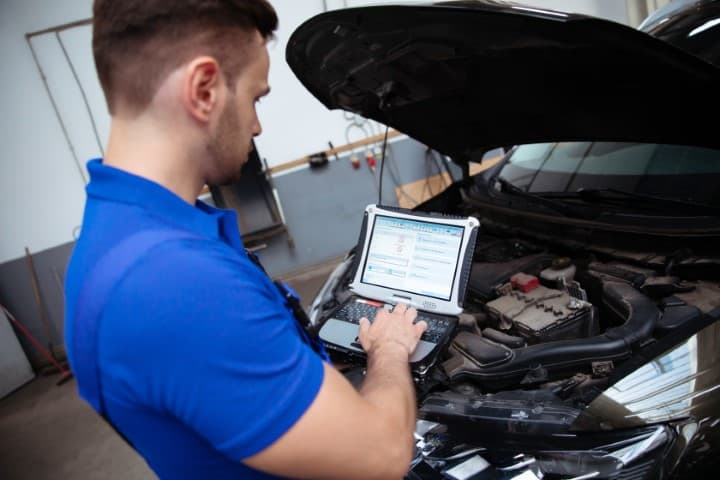 Young confident handsome car mechanic with laptop in hand conducts computer diagnostics for errors in the car systems